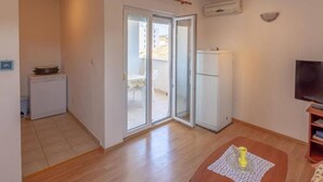 A compact living space with a kitchenette, a sliding glass door leading to a balcony, a refrigerator, and a television. - Charming and Cozy Okrug Gornji Apartment With Balcony (Okrug)