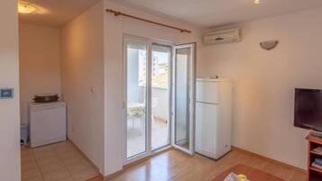 Ein kompakter Wohnbereich mit Küchenzeile, einer Schiebetür zu einem Balkon, einem Kühlschrank und einem Fernseher.