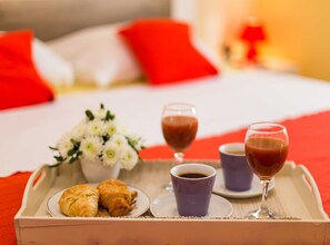Ein Frühstücksbrett mit Croissants, Kaffeetassen und einem Glas roter Flüssigkeit auf einem Bett mit roten Kissen.