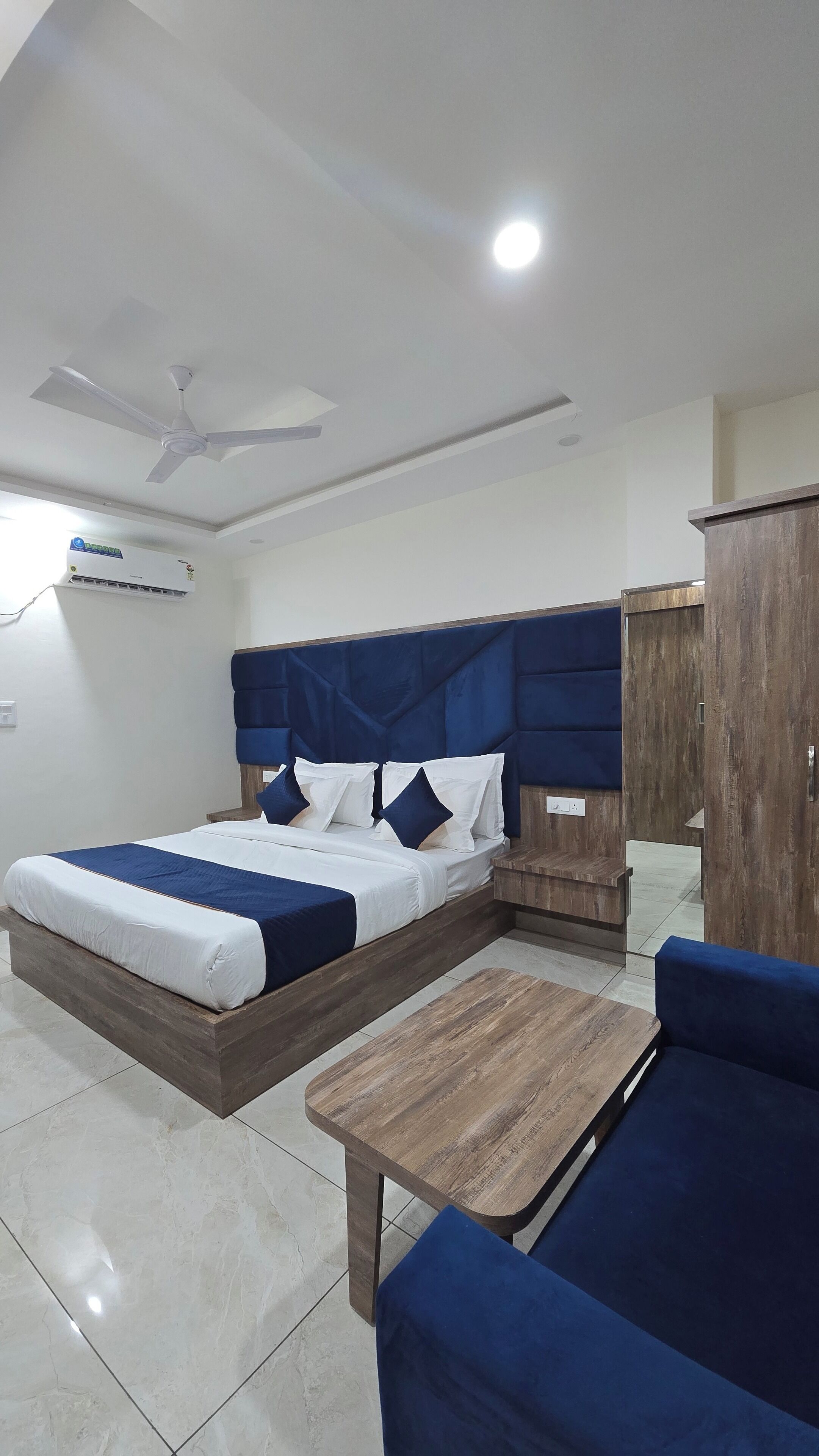 Un dormitorio con cama, mesita de noche de madera, armario de madera, sofá tapizado azul y ventilador de techo.