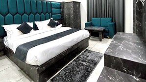 Quarto moderno com cama grande, cabeceira escura, área de estar com sofá e parede de destaque em mármore.