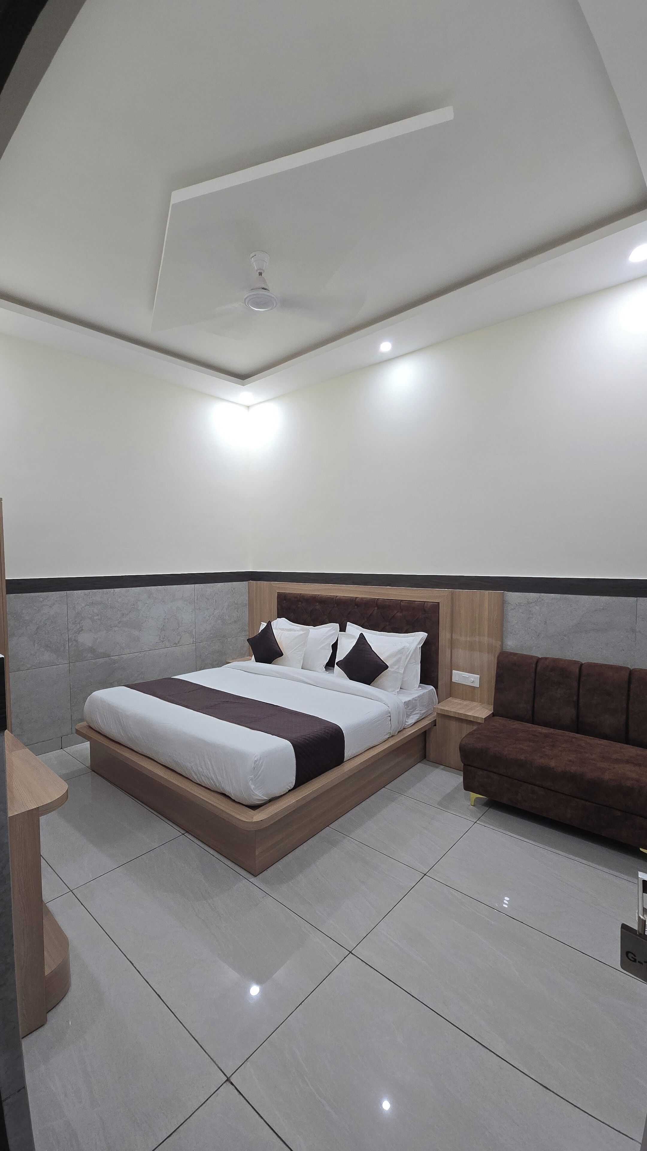 Una habitación de hotel moderna con una cama grande, un cabecero de madera, un sofá marrón y una mesita de noche pequeña.