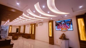 Uma área de recepção de hotel com design moderno, incluindo um balcão de atendimento, espaço de estar e uma tela grande exibindo uma imagem decorativa.
