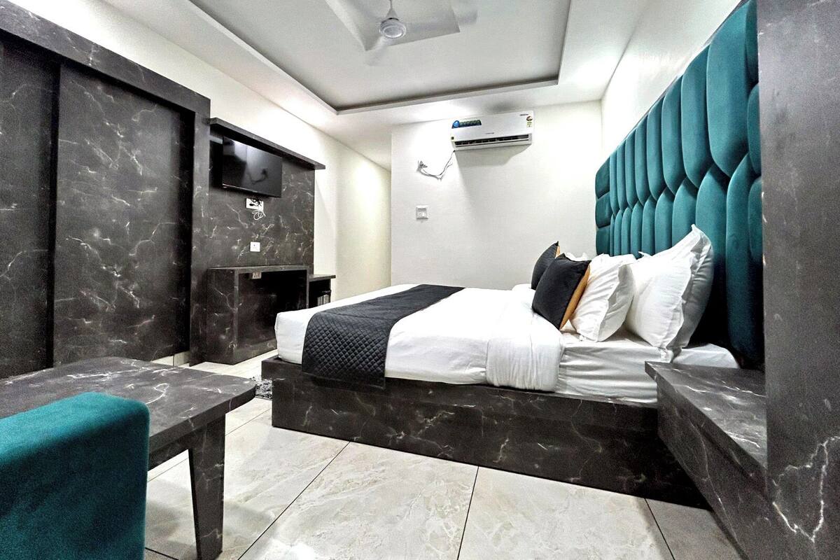 Una habitación de hotel moderna con suelo de mármol, una cama con cabecero capitonado, un televisor de pantalla plana y un equipo de aire acondicionado.