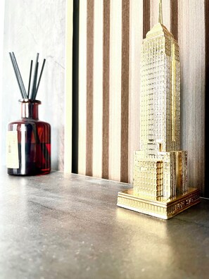 A model of a tall building with a detailed facade, a red vase with black sticks, and a textured wall in the background.
