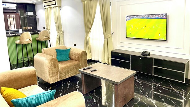 Egy modern nappali, amelyben egy kanapé, egy dohányzóasztal és egy televízió található, melyen egy sportmérkőzést közvetítenek.