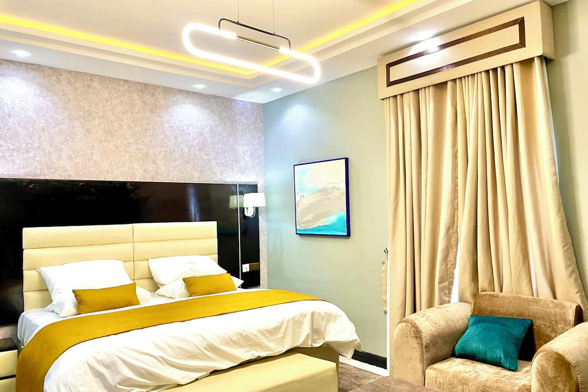 A modern hotel room with a large bed, a bedside table, a chair, and a painting on the wall.