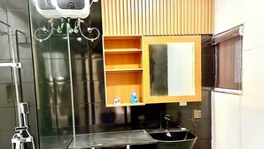 Un baño moderno con cabina de ducha de vidrio, un lavabo negro y un tocador de madera con espejo.