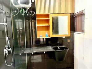 A modern bathroom with a glass shower enclosure, a black sink, and a wooden vanity with a mirror.