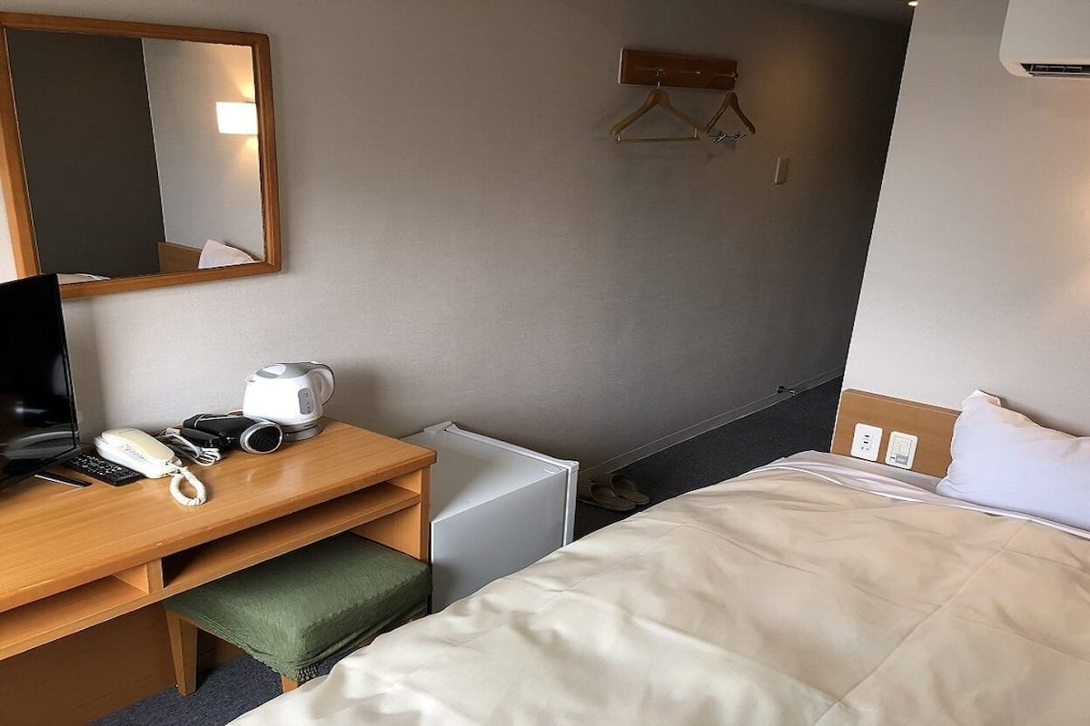 Habitación de hotel con cama, escritorio, teléfono, tetera y espejo.