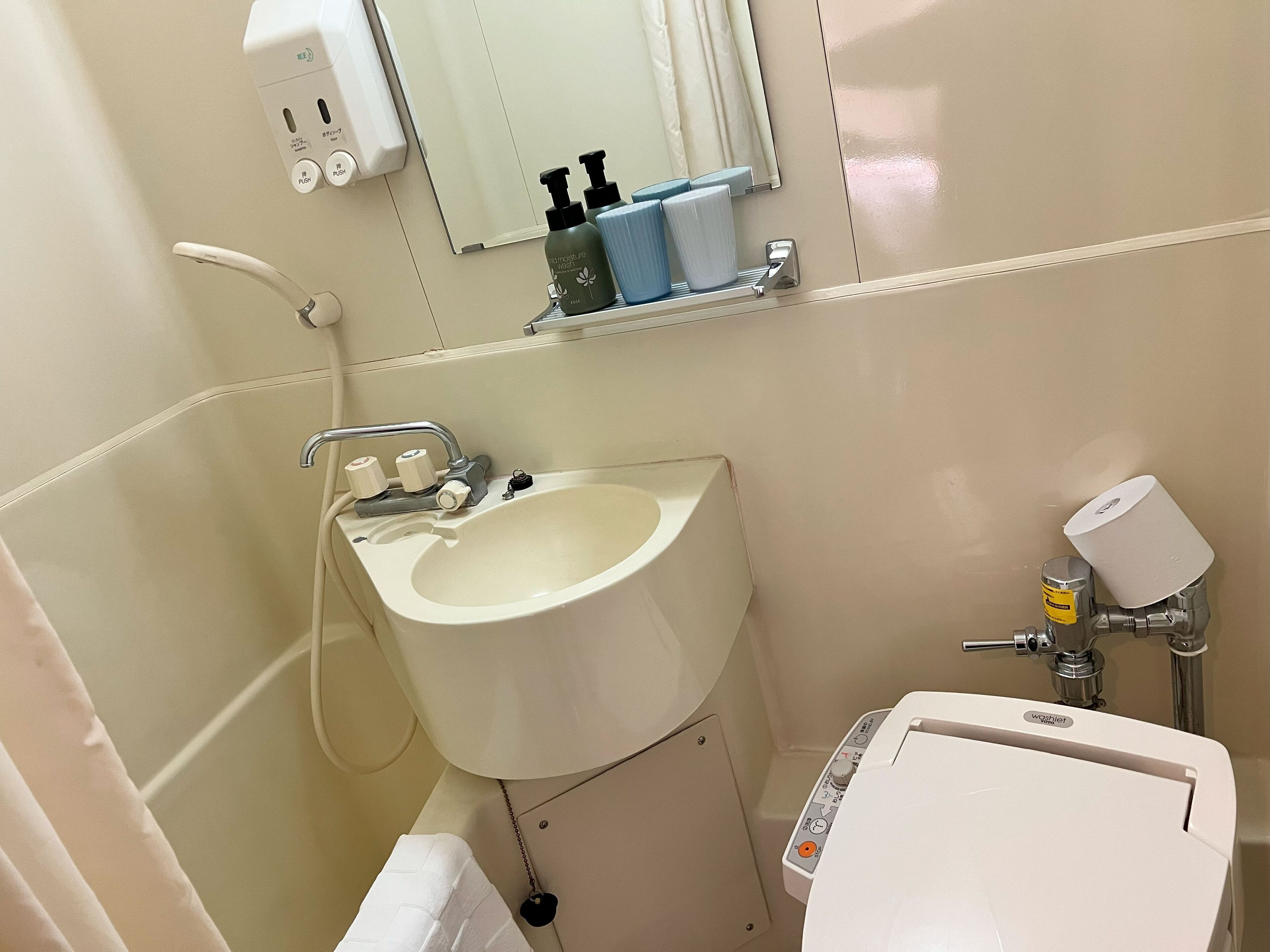 Un baño con lavamanos, espejo, dispensador de jabón e inodoro.