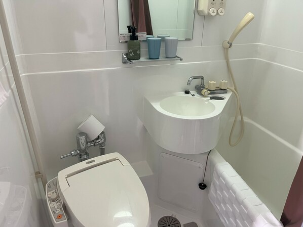 Un baño con lavamanos, inodoro y bañera blancos. Hay un espejo sobre el lavamanos y un estante con artículos de aseo.