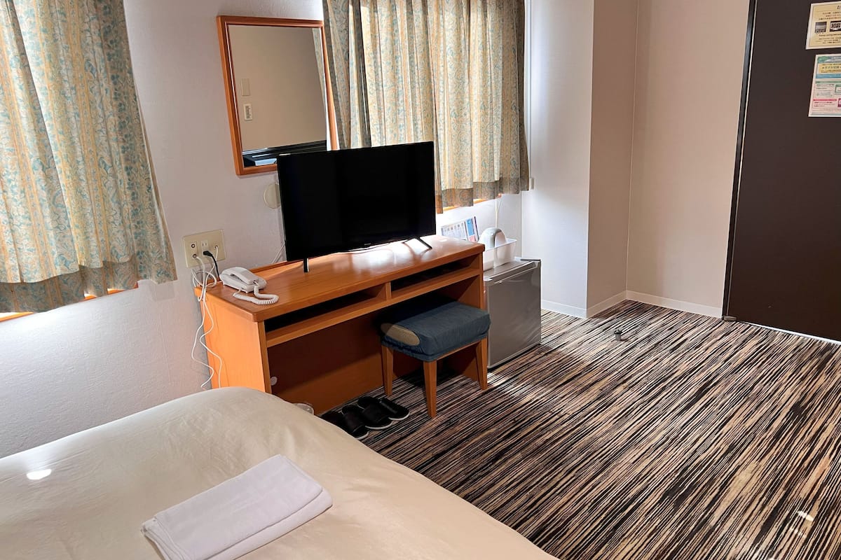 Habitación de hotel con cama, escritorio, computadora, teléfono, refrigerador pequeño y espejo.