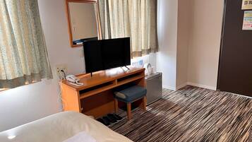 A hotel room with a bed, a desk with a computer, a telephone, a small refrigerator, and a mirror.