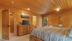 A wooden cabin bedroom with a bed, dresser, TV, and a door leading outside. - 30 Min to Jackson Hole • Alpine Retreat • Hot Tub • Sleeps 12 (Alpine)