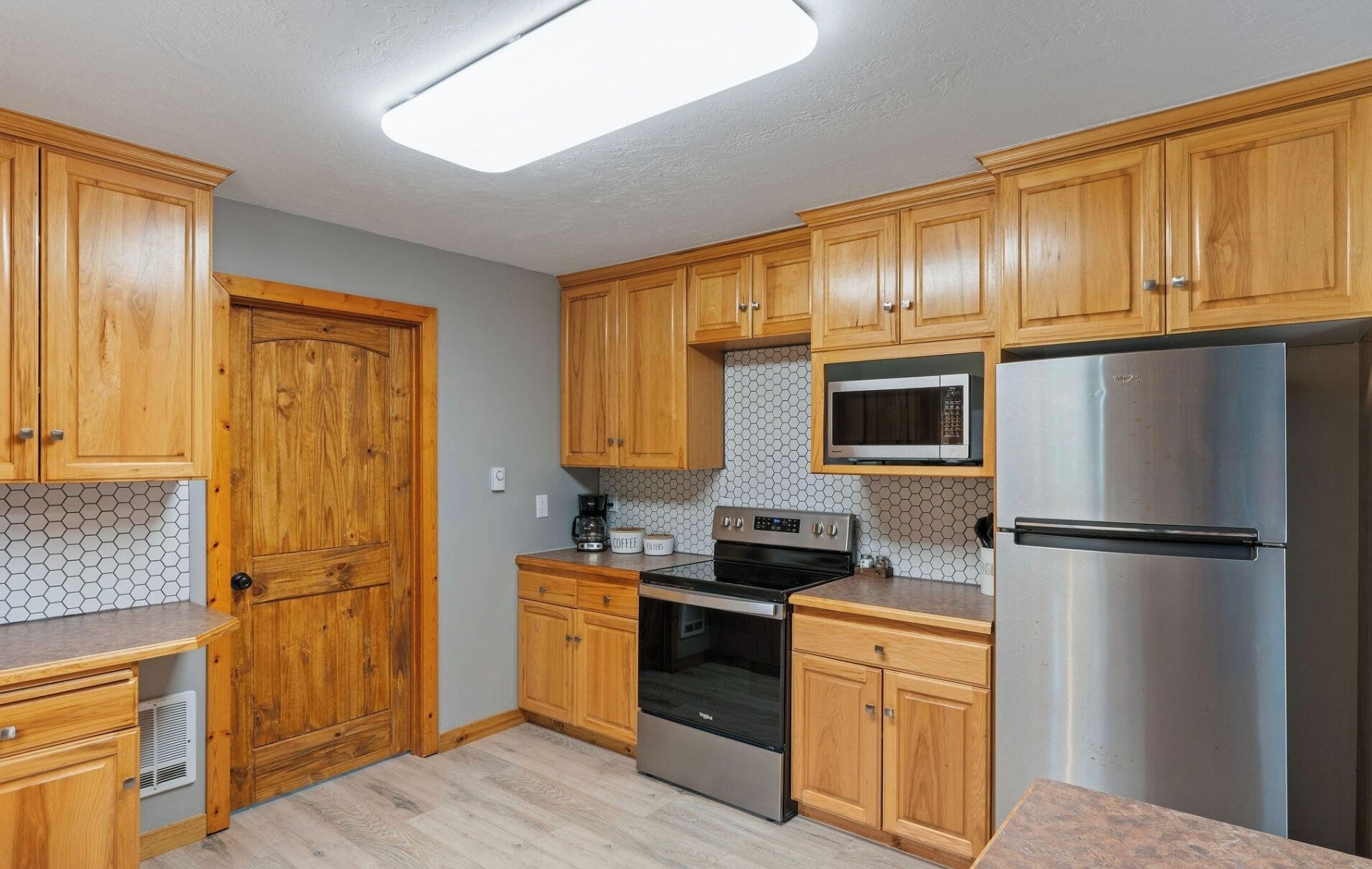 A kitchen with wooden cabinets, a microwave, a stainless steel refrigerator, and an oven.