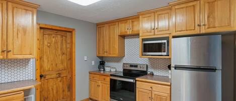 A kitchen with wooden cabinets, a microwave, a stainless steel refrigerator, and an oven.