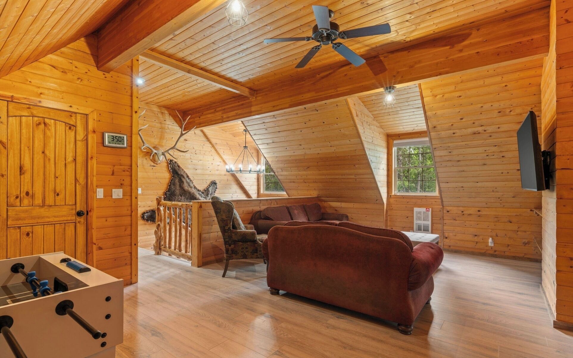 Ein gemütliches Blockhaus-Interieur mit Holzboden, Deckenventilator, Kamin, Sofa und Esstisch.