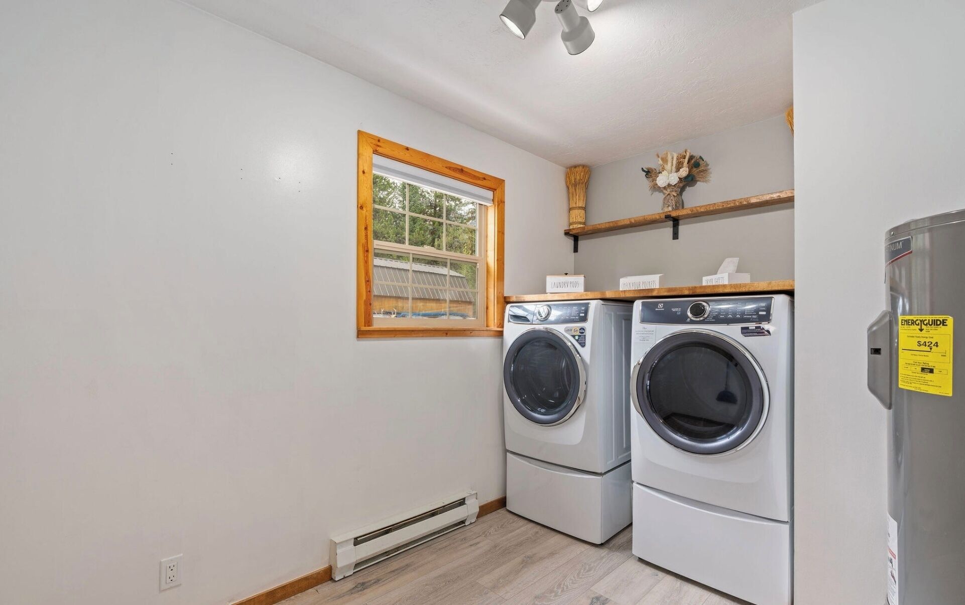 A laundry room with two stacked front-loading washing machines, a window with a wooden frame, and a shelf with laundry supplies.