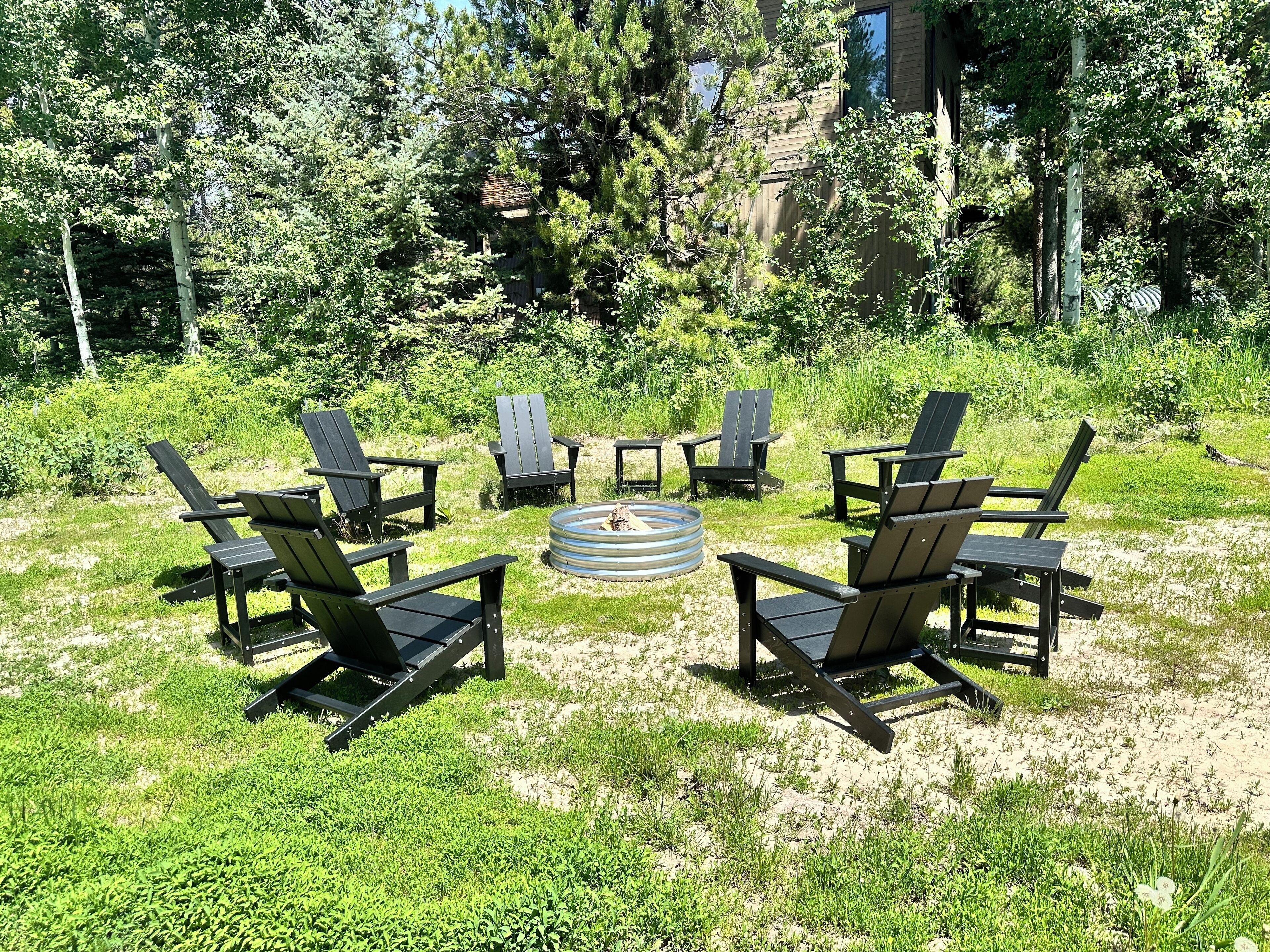 An outdoor seating area with six Adirondack chairs arranged around a circular fire pit.