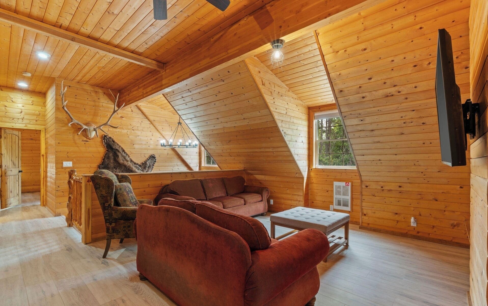 A cozy cabin interior with a wooden ceiling, a sofa, a chair, and a deer antler decoration.