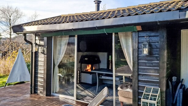 Een houten chalet met een glazen deur die leidt naar een terras, een open haard en een kleine tafel.