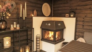 Een knus vertrek met een open haard, een tafel en een plank met kaarsen en decoratieve objecten.