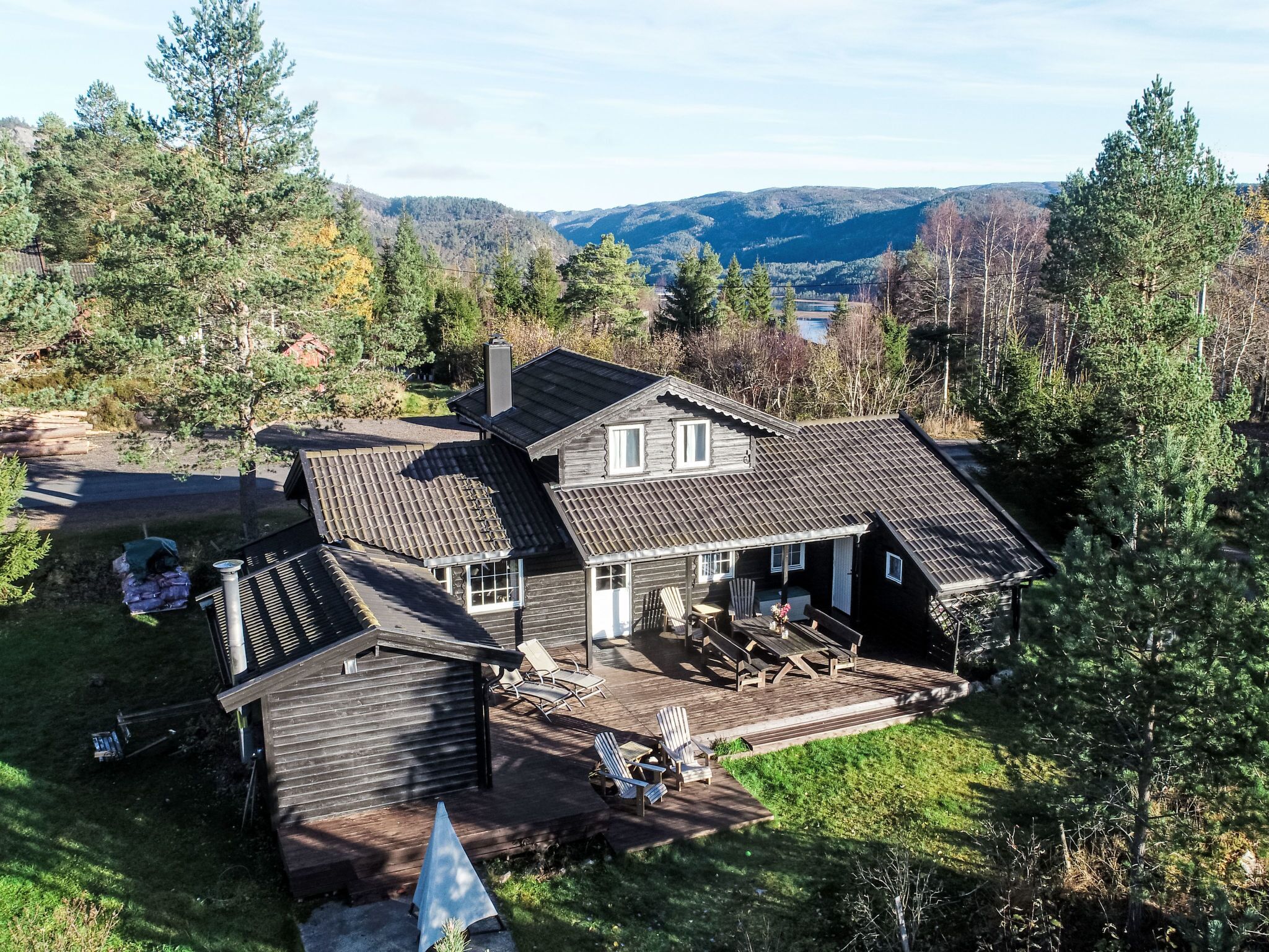 A wooden house with a sloped roof, a covered patio with outdoor furniture, and a view of a forested valley.
