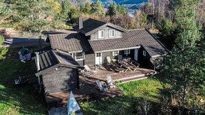 Een houten huis met een schuin dak, een overdekt terras met tuinmeubilair en uitzicht op een bebost dal.