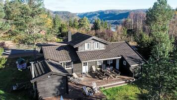 A wooden house with a sloped roof, a covered patio with outdoor furniture, and a view of a forested valley.