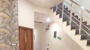 Um hall de hotel com uma escadaria, uma porta de madeira, um papel de parede estampado e um chão de azulejos.