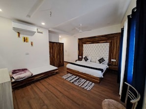 A bedroom with a bed, a small sofa, wooden flooring, a ceiling fan, and an air conditioning unit. - Hotel D Plaza (Dera Bassi)