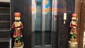 Entrada de hotel com piso de mármore, uma escadaria e duas estátuas decorativas.
