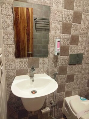 A bathroom with a white sink, a mirror, a towel rack, a soap dispenser, and a toilet. - Hotel D Plaza (Dera Bassi)