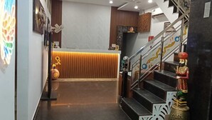 Uma área de recepção de hotel com design moderno, apresentando um balcão de atendimento, uma escadaria com detalhes decorativos e um painel de parede com padrão.