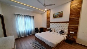 Quarto com cama, piso de madeira, ventilador de teto, mesa de cabeceira, cadeira e janela com cortinas.