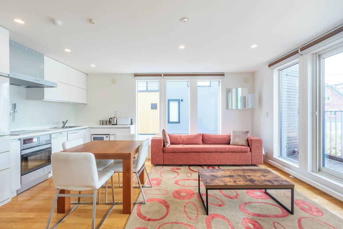 A modern kitchen with white cabinets, a wooden dining table, and a red sofa.