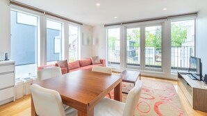 A modern living room with a wooden dining table, white chairs, a red sofa, and large windows offering a view of the outside. - Hangetsu Niseko (Kutchan)