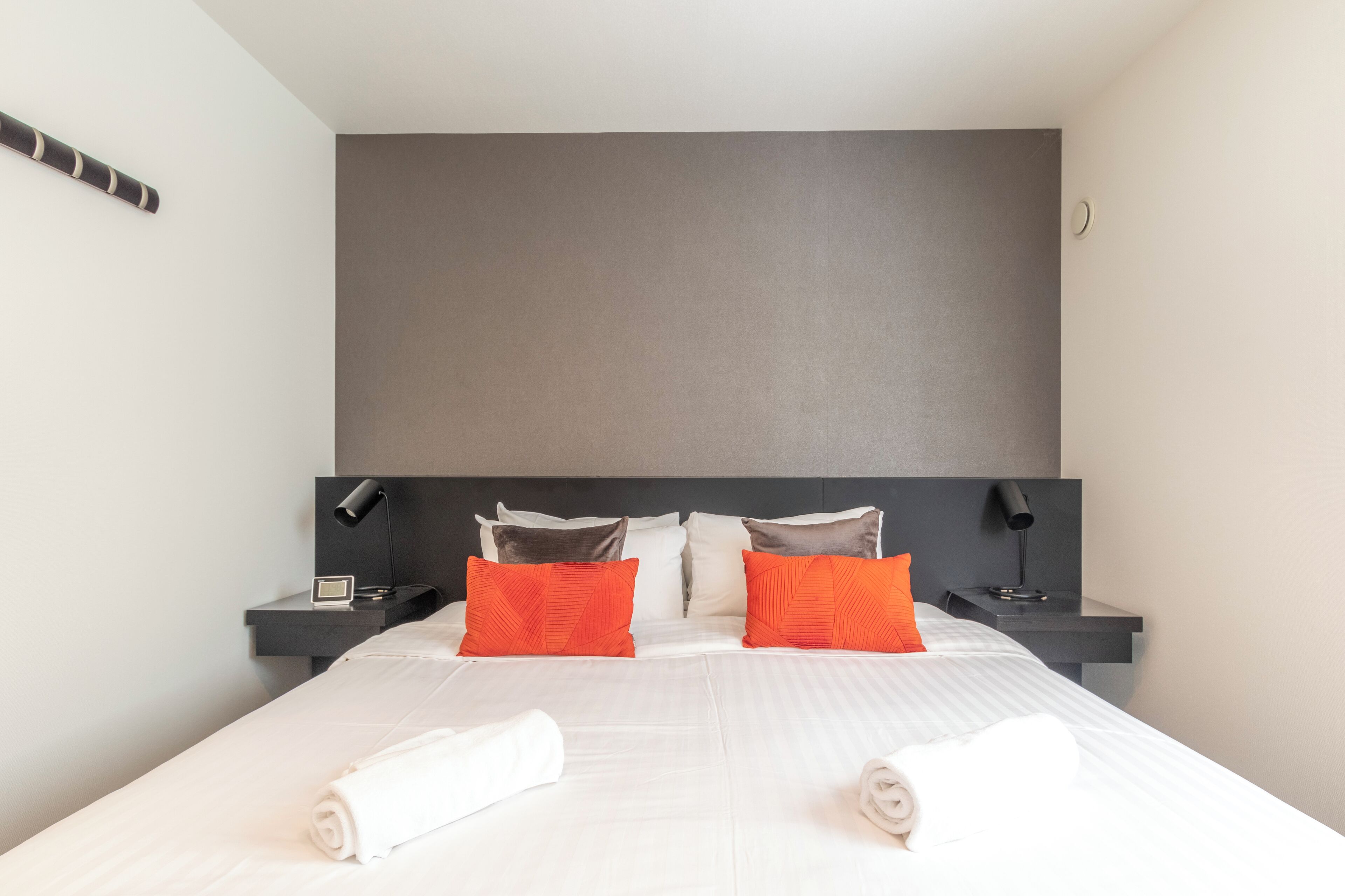 A modern hotel room with a large bed, two nightstands, and a dark headboard.