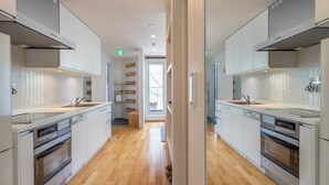 A modern kitchen with white cabinetry, built-in ovens, and a wooden floor. - Hangetsu Niseko (Kutchan)