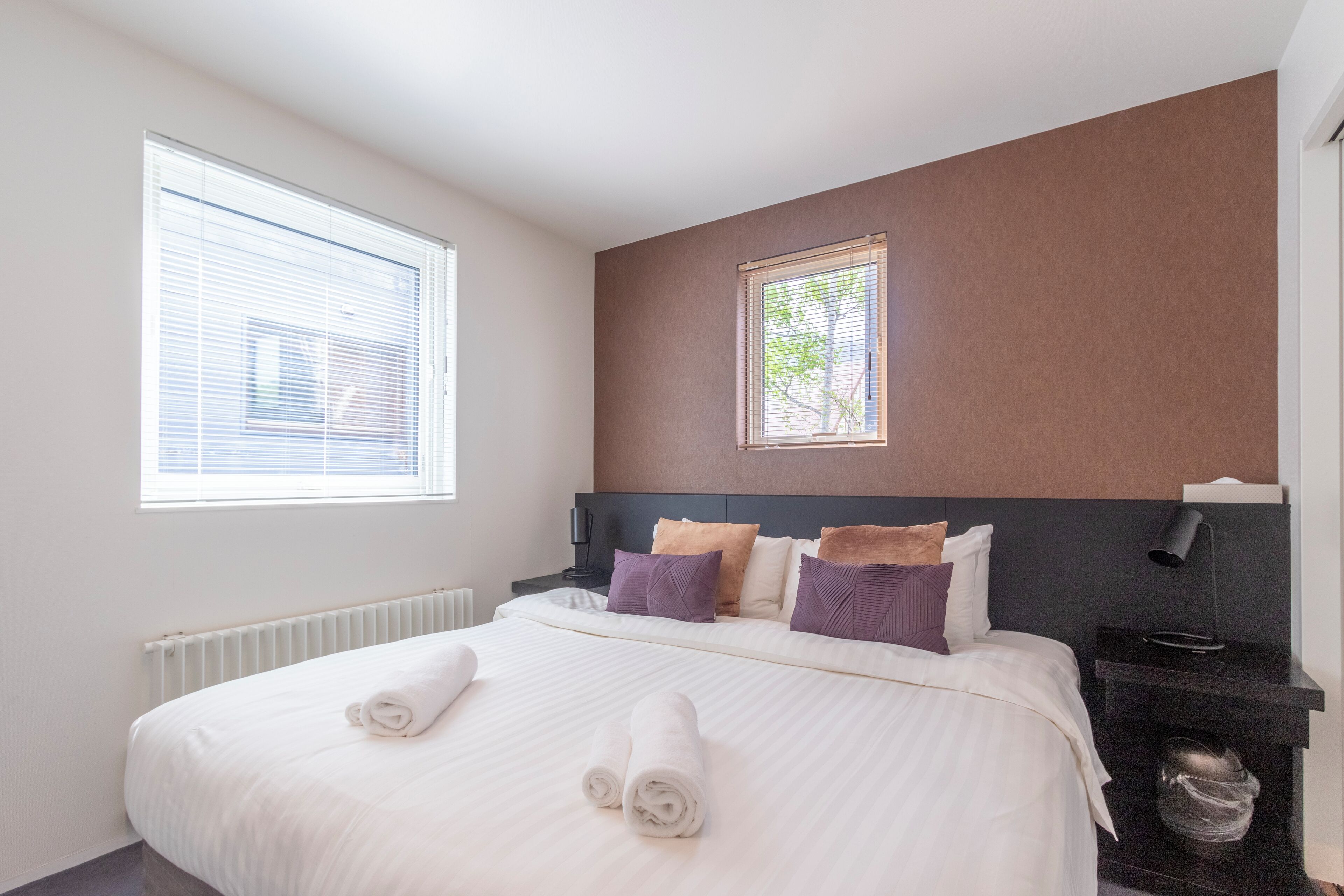 A hotel room with a large bed, a nightstand, a window, and a radiator.