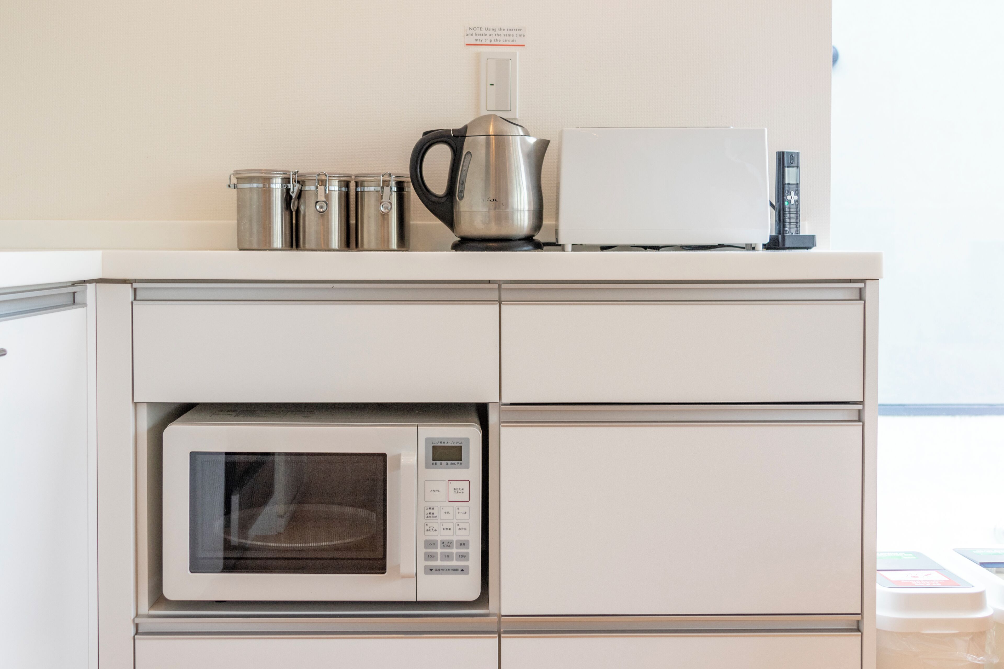 A kitchen with a microwave, a kettle, and a coffee maker on the countertop.