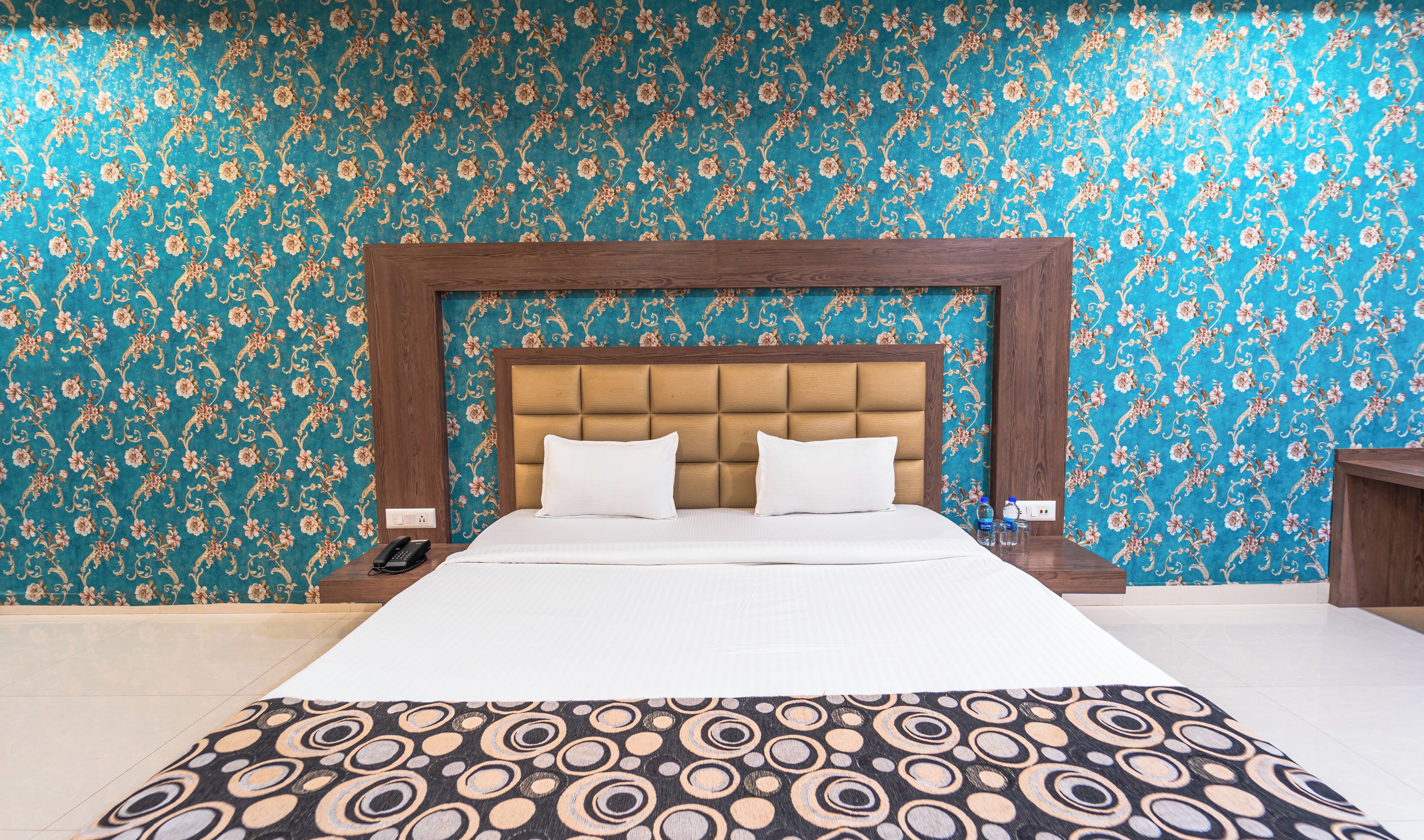 A hotel room with a large bed, a wooden headboard, and a floral patterned wall.