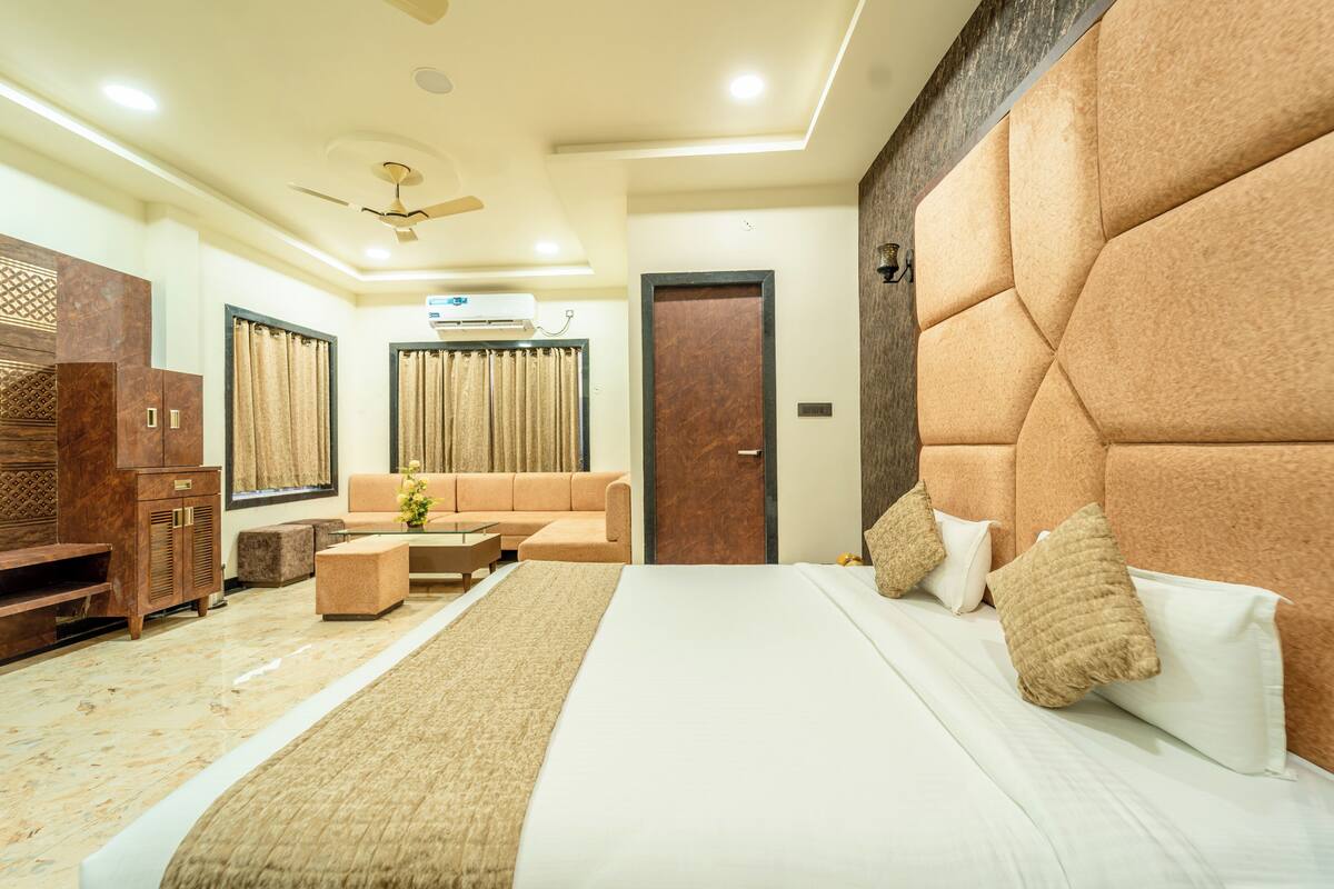 A modern hotel room with a large bed, a sofa, a wooden cabinet, and a ceiling fan.