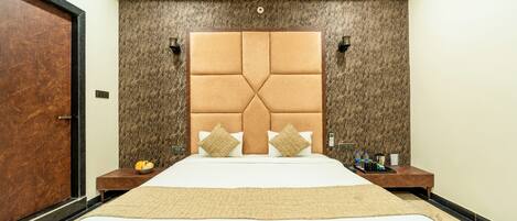 Una habitación de hotel con una cama grande, una puerta de madera, una pared de mármol y una mesita de noche con una lámpara y un atril con artículos de tocador.