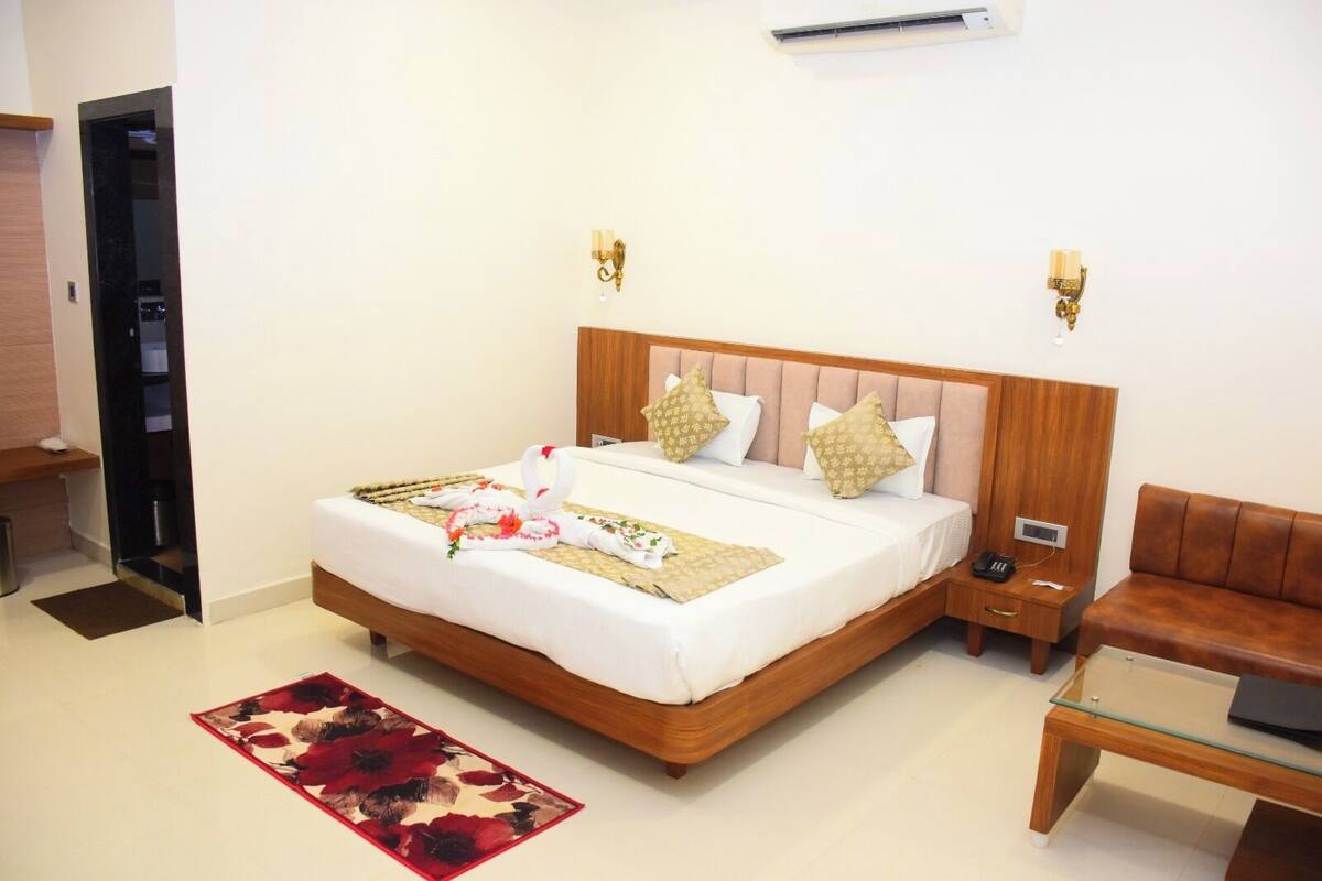A hotel room with a wooden bed, two wall-mounted lamps, a bedside table with a phone, and a red floral rug.