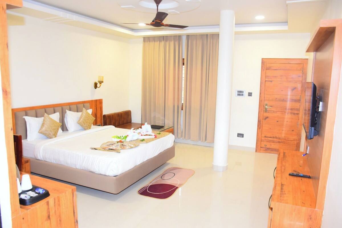A hotel room with a large bed, a TV, a wooden wardrobe, and a ceiling fan.