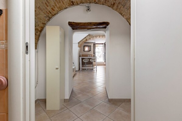 A hallway with a tiled floor, an arched brick ceiling, and a door leading to a room with a window.