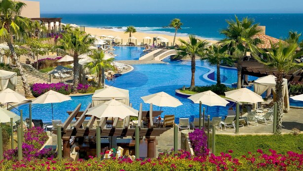 Un resort con piscina, playa, palmeras y vista al océano.