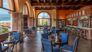 Zona de bar con asientos, vistas al océano y barra con diferentes botellas.